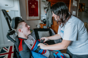 A boy in a wheelchair being strapped into a hoist by his mum.